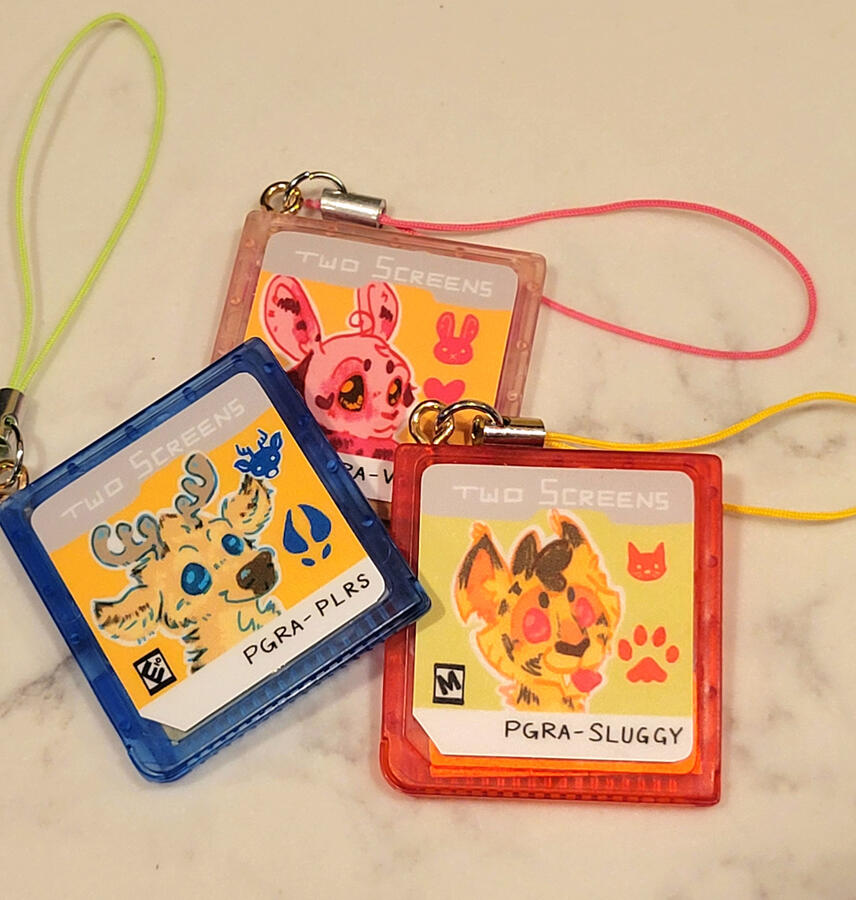 game cart phone charms -- CONTAINS NO REAL MOTHERBOARD. IT IS PAINTED SHRINKY DINK. custom 3D models and sticker sizing done in-house, outsourced for print, and returned to in-house for asembly.